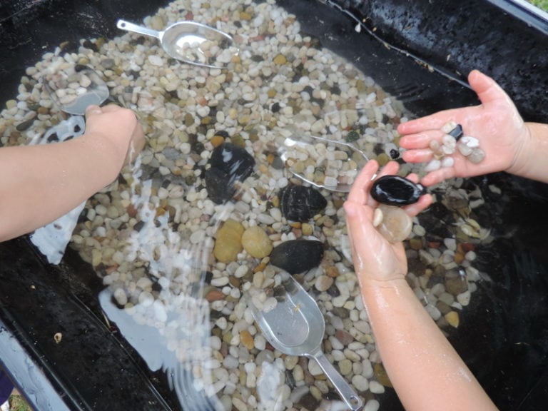 a sensory water tub tray with small pebbles and scoops children are exploring