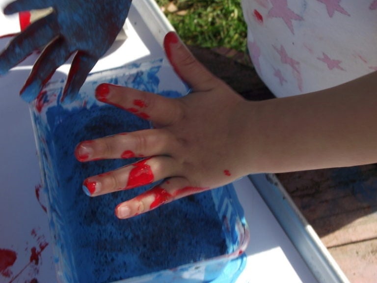 child with paint stained hands pressing into homemade paint sponge trays for stamping