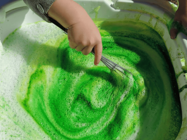 toddler whisking bubbles in a water sensory tub with green colour mixing fine motor