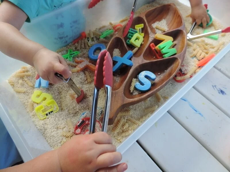 rice sensory play tray with magnetic letters and tongs